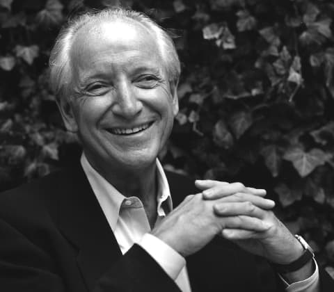A portrait of designer Michael Graves smiling with hands interlocked